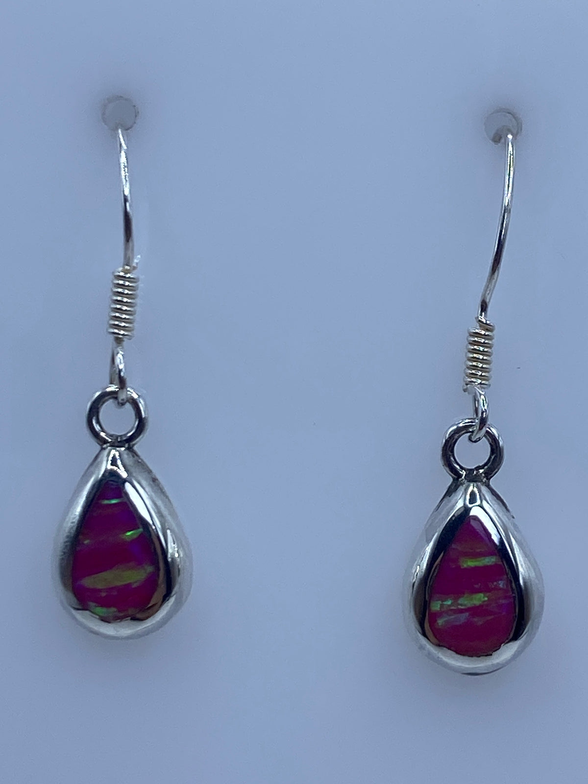 Aretes colgando sobre fondo azul, vista lateral del engaste y el gancho de plata