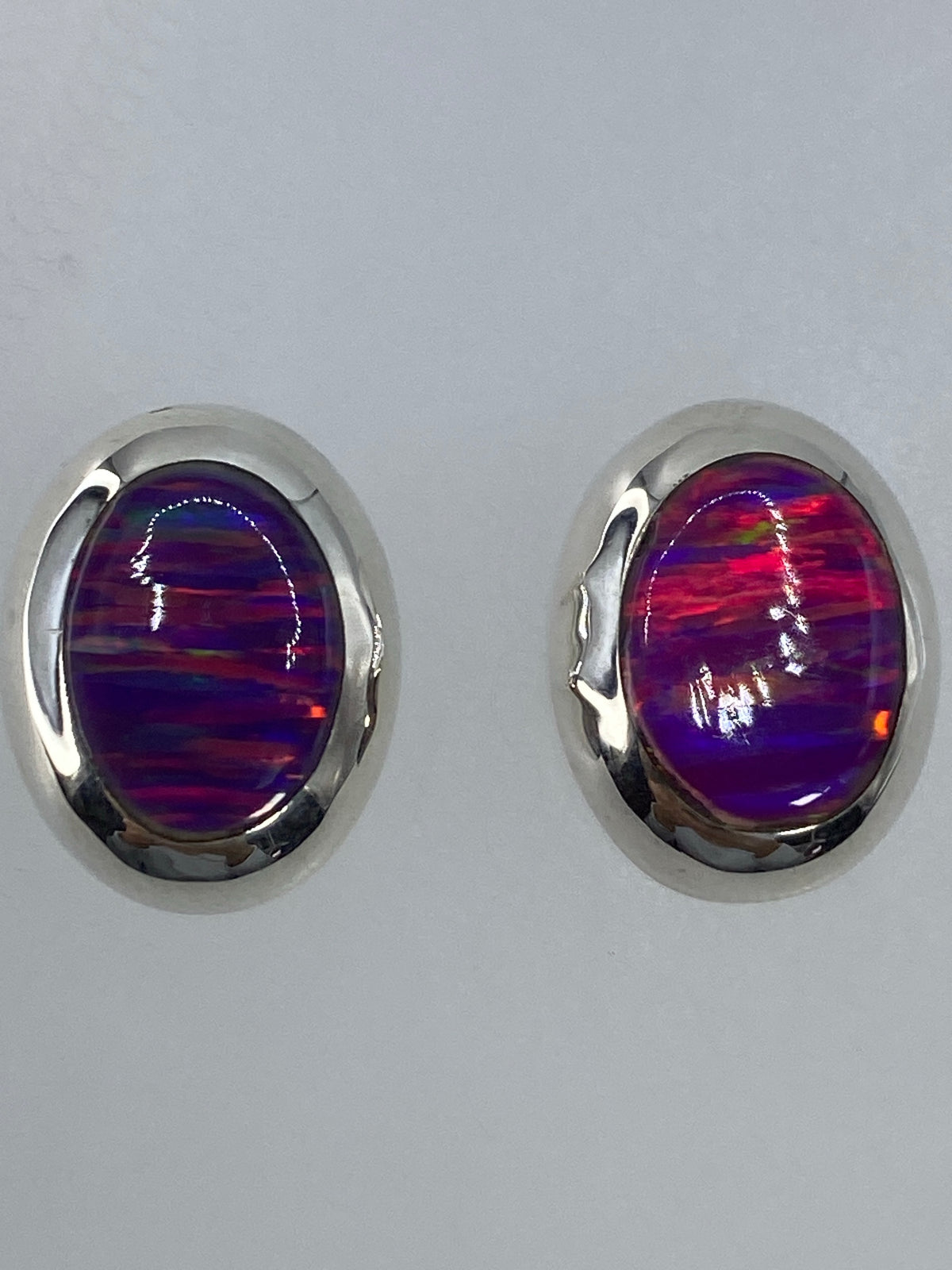 Aretes de plata con ópalo de fuego sobre escala de medidas, mostrando tamaño real de 1.3 cm