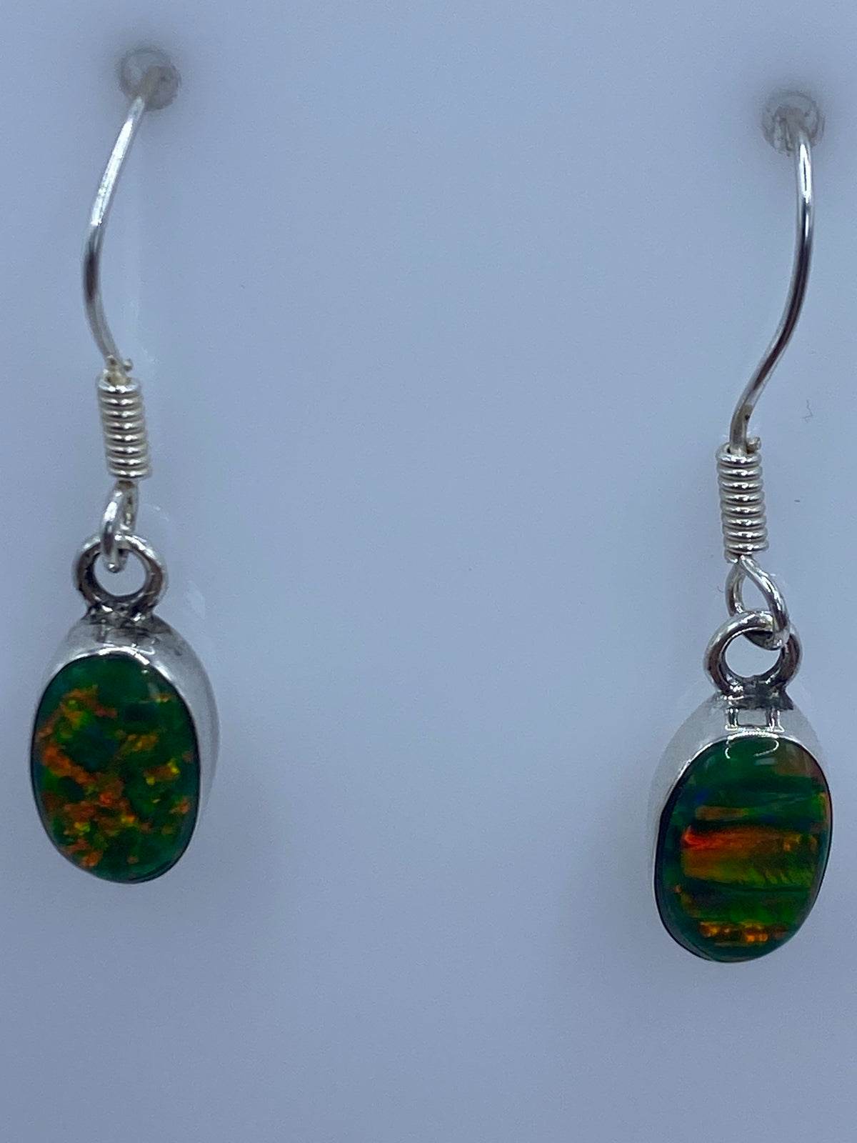 Detalle de un arete mostrando el engaste a mano del ópalo de fuego con tonos verde limón