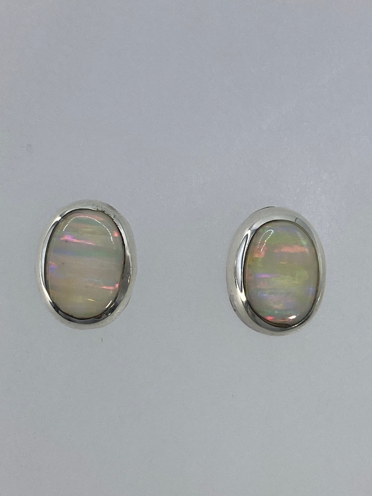 Par de aretes de plata con ópalo de fuego multicolor engastados a mano, mostrando reflejos rojo, naranja y azul
