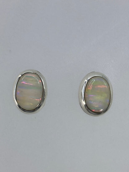 Par de aretes de plata con ópalo de fuego multicolor engastados a mano, mostrando reflejos rojo, naranja y azul