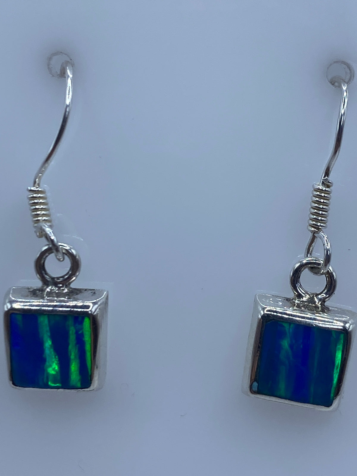 Los dos aretes juntos en vista frontal, brillo azul del ópalo visibles