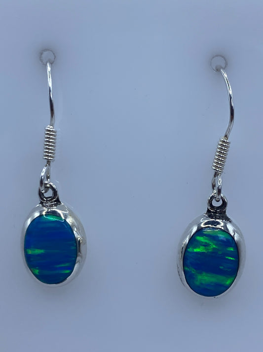 Par de aretes de plata con ópalo de fuego azul cielo, colgando sobre fondo blanco