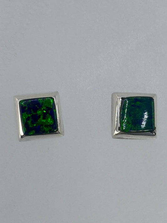 Par de aretes de plata con ópalo de fuego verde, vistos de frente sobre superficie blanca