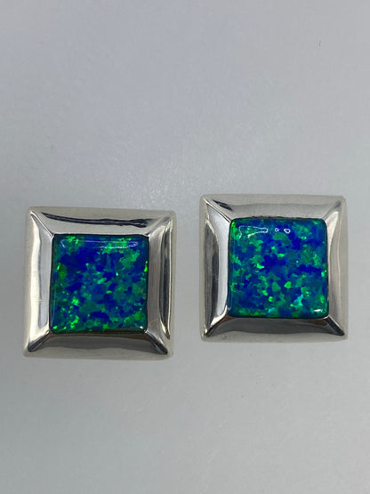 Par de aretes de plata con ópalo de fuego multicolor en estuche, mostrando los destellos verdes y azules de la piedra