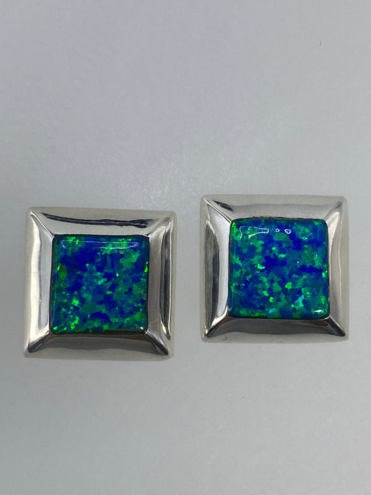 Par de aretes de plata con ópalo de fuego multicolor en estuche, mostrando los destellos verdes y azules de la piedra