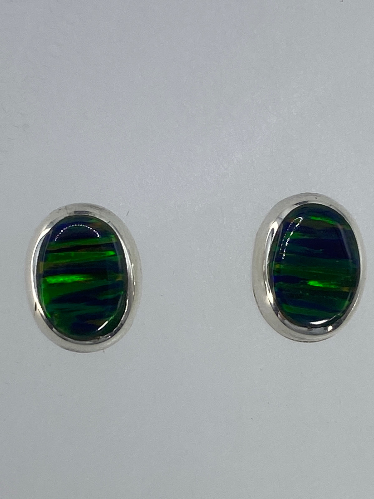 Par de aretes de plata con ópalo de fuego verde engastado, sobre fondo blanco