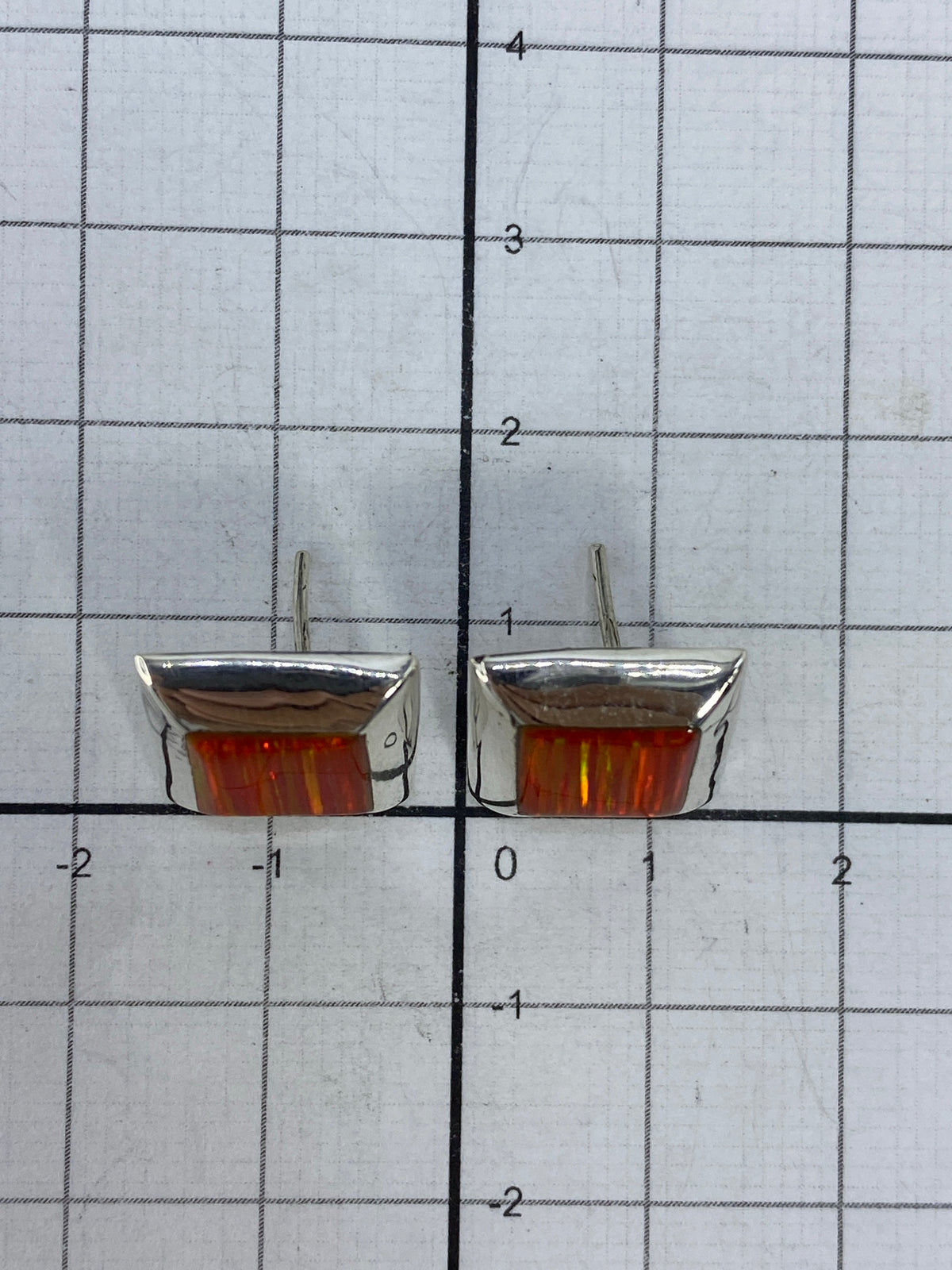 Aretes de ópalo de fuego colgando, luz natural resaltando el color naranja