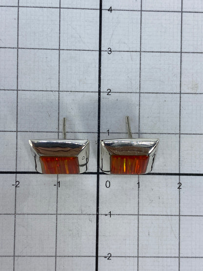 Aretes de ópalo de fuego colgando, luz natural resaltando el color naranja