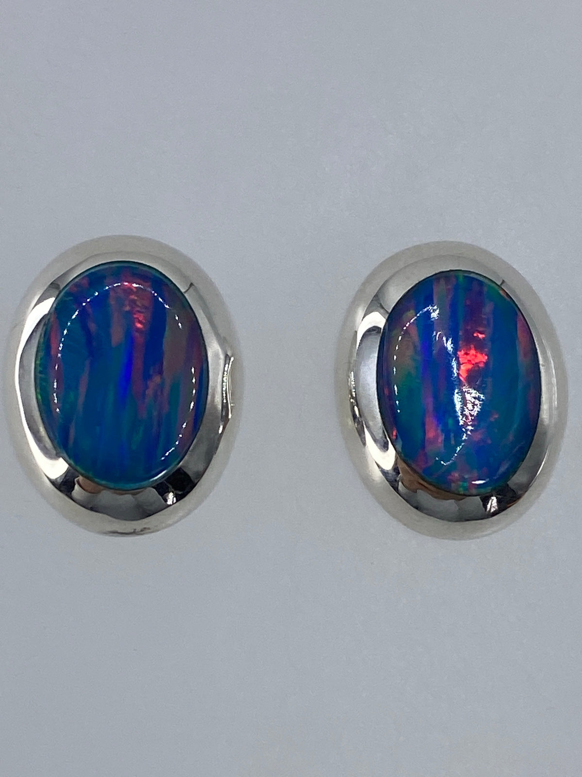 Aretes con ópalo de fuego reflejando luz, mostrando los colores rojo, naranja y azul