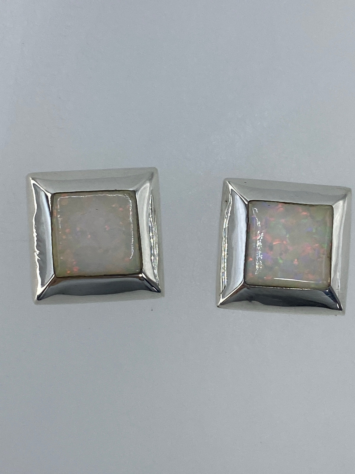 Par de aretes de plata con ópalo de fuego multicolor engastado, luz natural mostrando destellos rojo y naranja