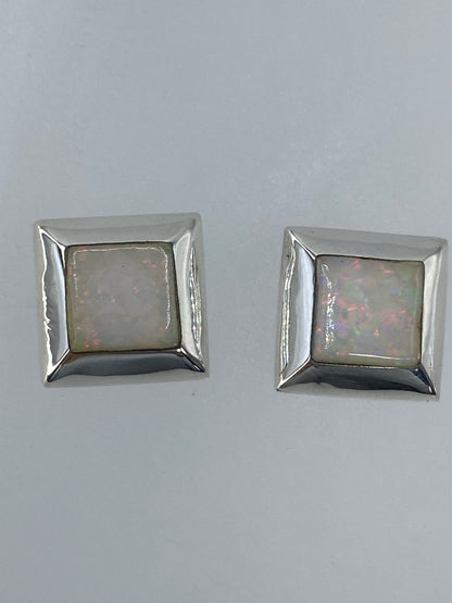 Par de aretes de plata con ópalo de fuego multicolor engastado, luz natural mostrando destellos rojo y naranja