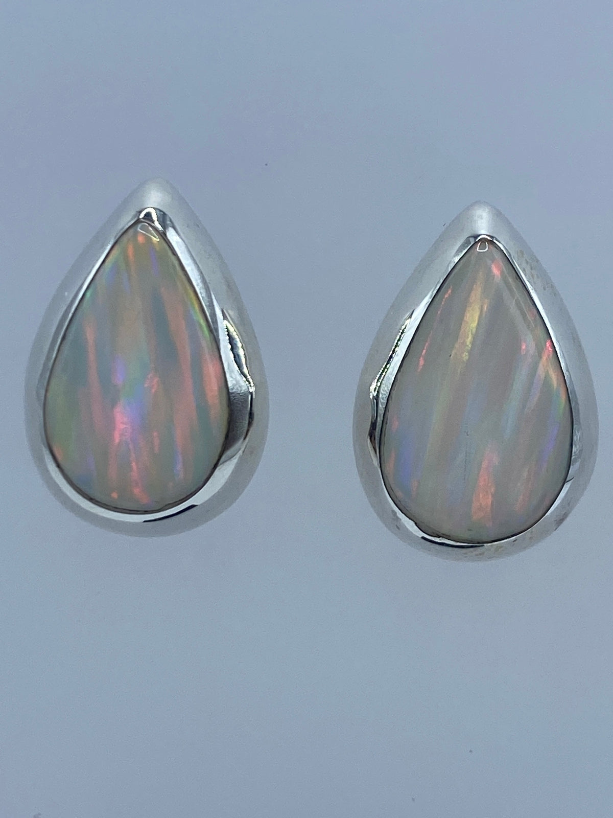 Par de aretes de plata con ópalo de fuego, mostrando reflejos multicolor rojo y naranja