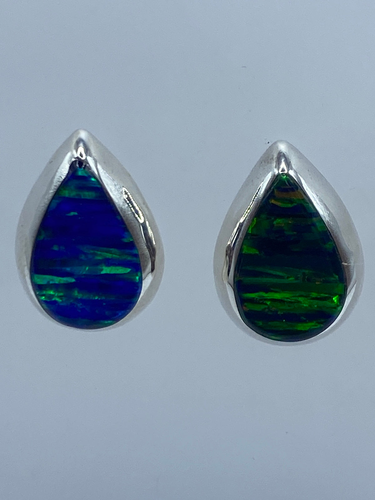 Detalle frontal de arete de plata 925 con ópalo de fuego engastado, luz reflejada en la piedra