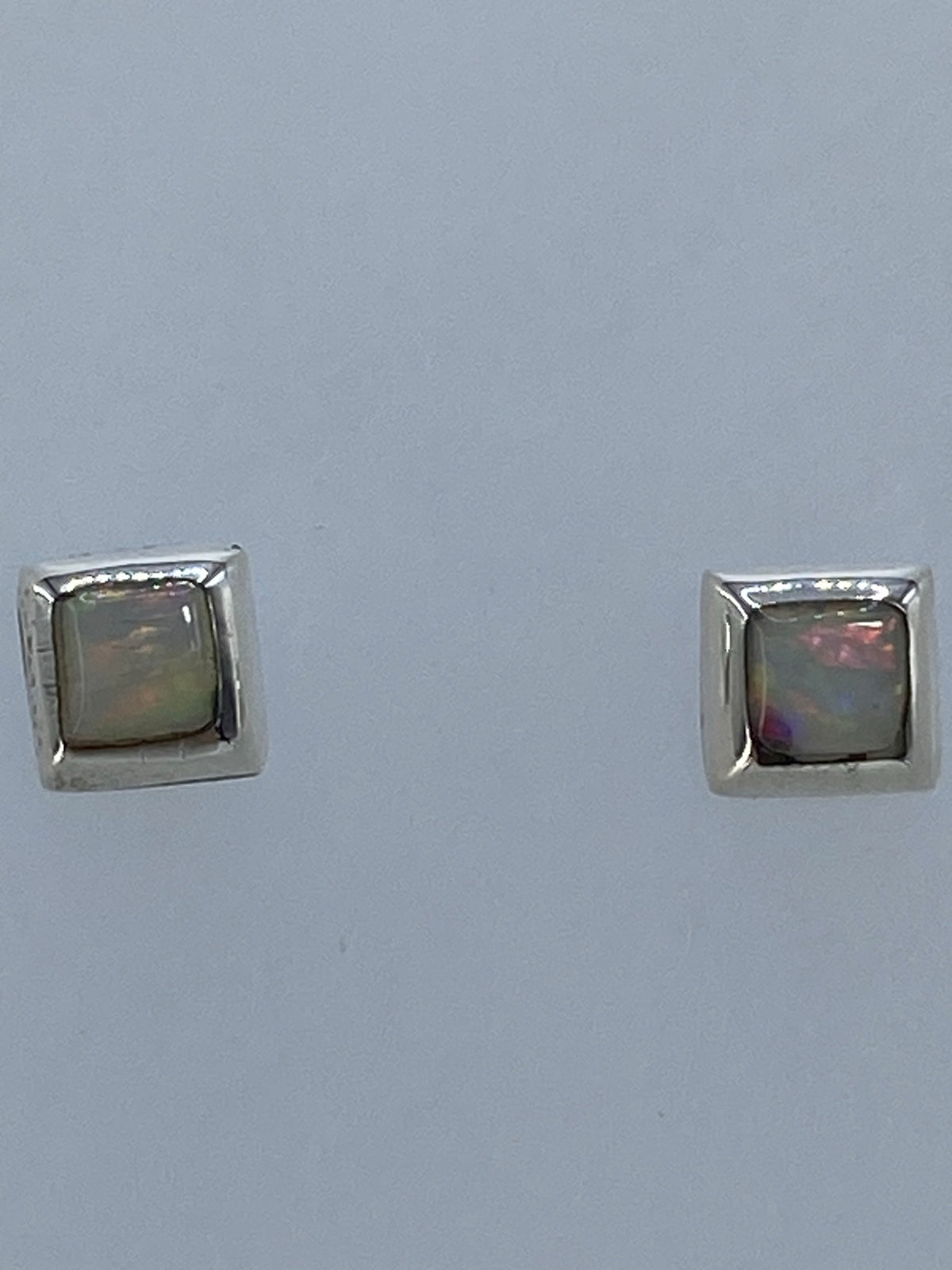 Detalle frontal de los aretes mostrando el juego de colores del ópalo de fuego