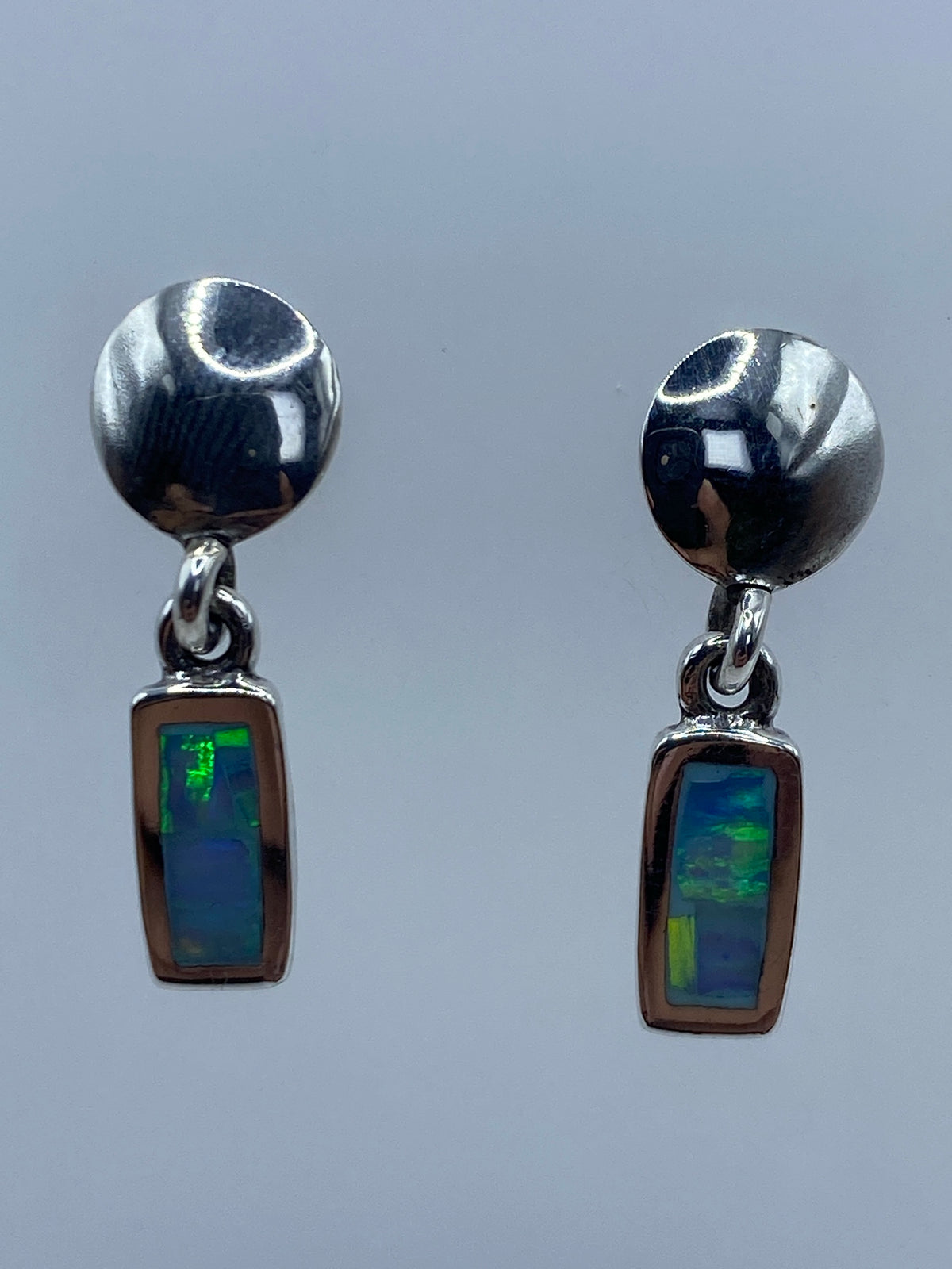 Aretes de plata con ópalo de fuego azul cielo engastado, par completo sobre fondo gris