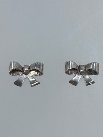 Par de aretes de plata en forma de moño minimalista, 1 cm de largo, sobre fondo gris