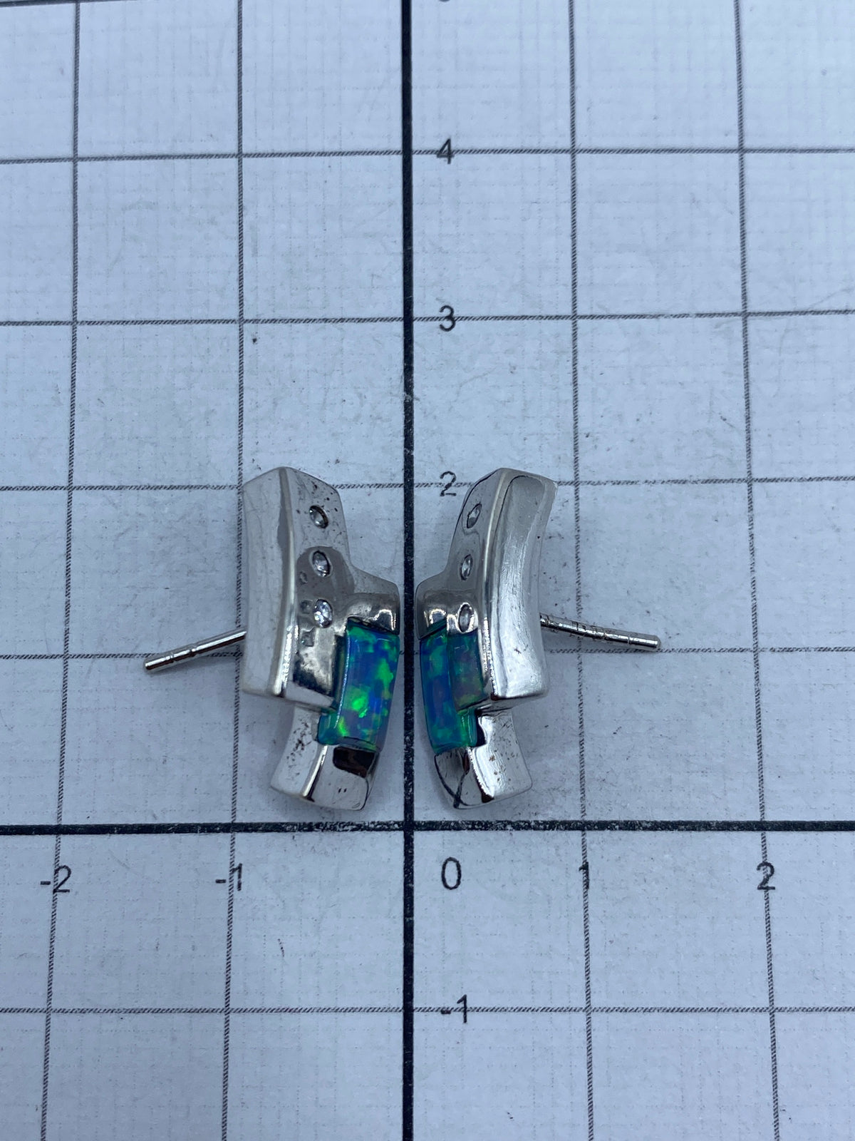 Aretes colgando sobre mesa blanca mostrando el tamaño real de 2 cm