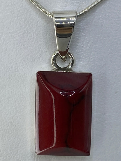 Detalle frontal del dije mostrando la incrustación de piedra roja pulida