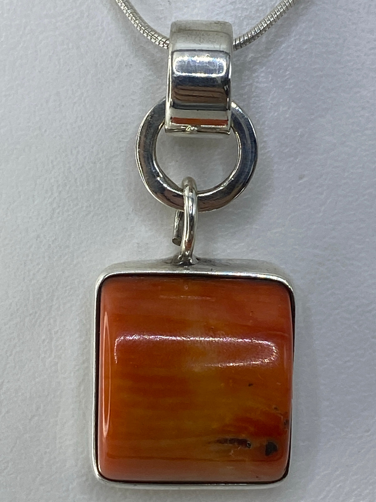 Dije cuadrado de plata 925 con piedra naranja engastada, colgando de cadena de plata