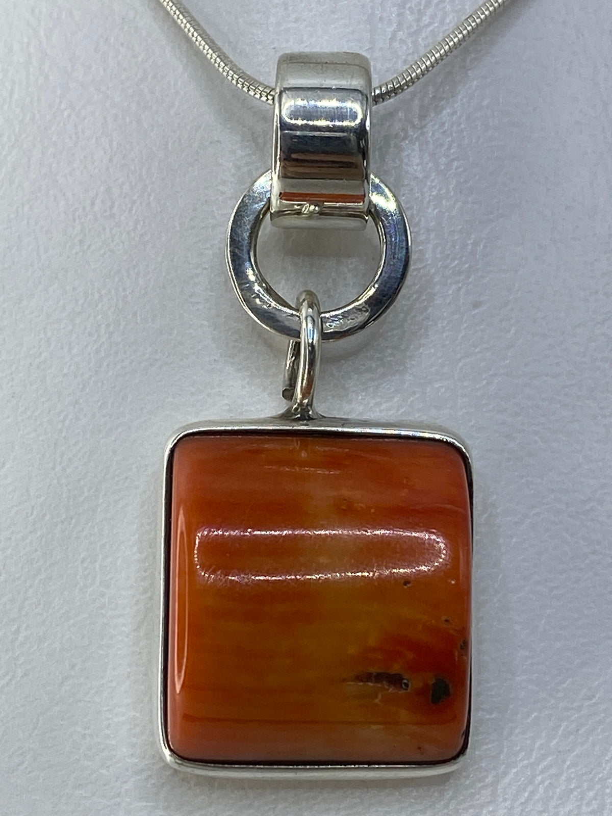 Vista frontal del dije de 3.8 cm con piedra naranja en bastidor de plata pulida
