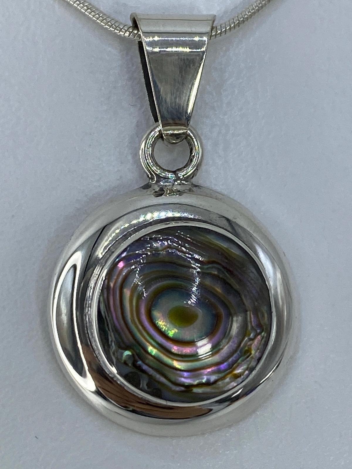 Dije de plata 925 con piedra multicolor reflejando luz, colgado de cadena de plata