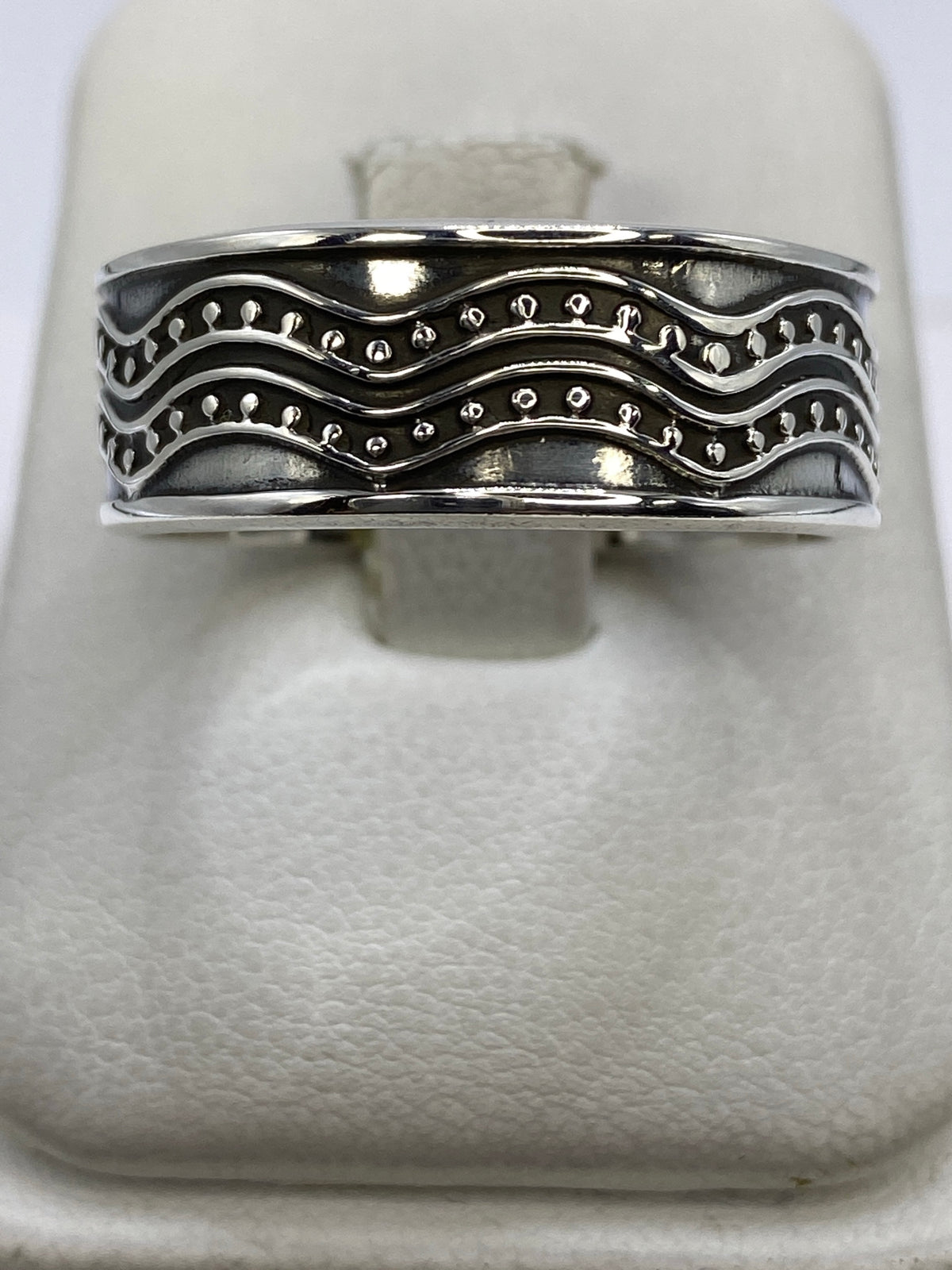 Anillo de plata repujado con ondas simétricas visto de frente en estuche blanco