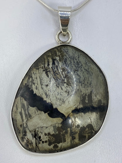 Dije de plata 925 con incrustación de piedra natural en tonos grises y negros, colgado de cadena plateada