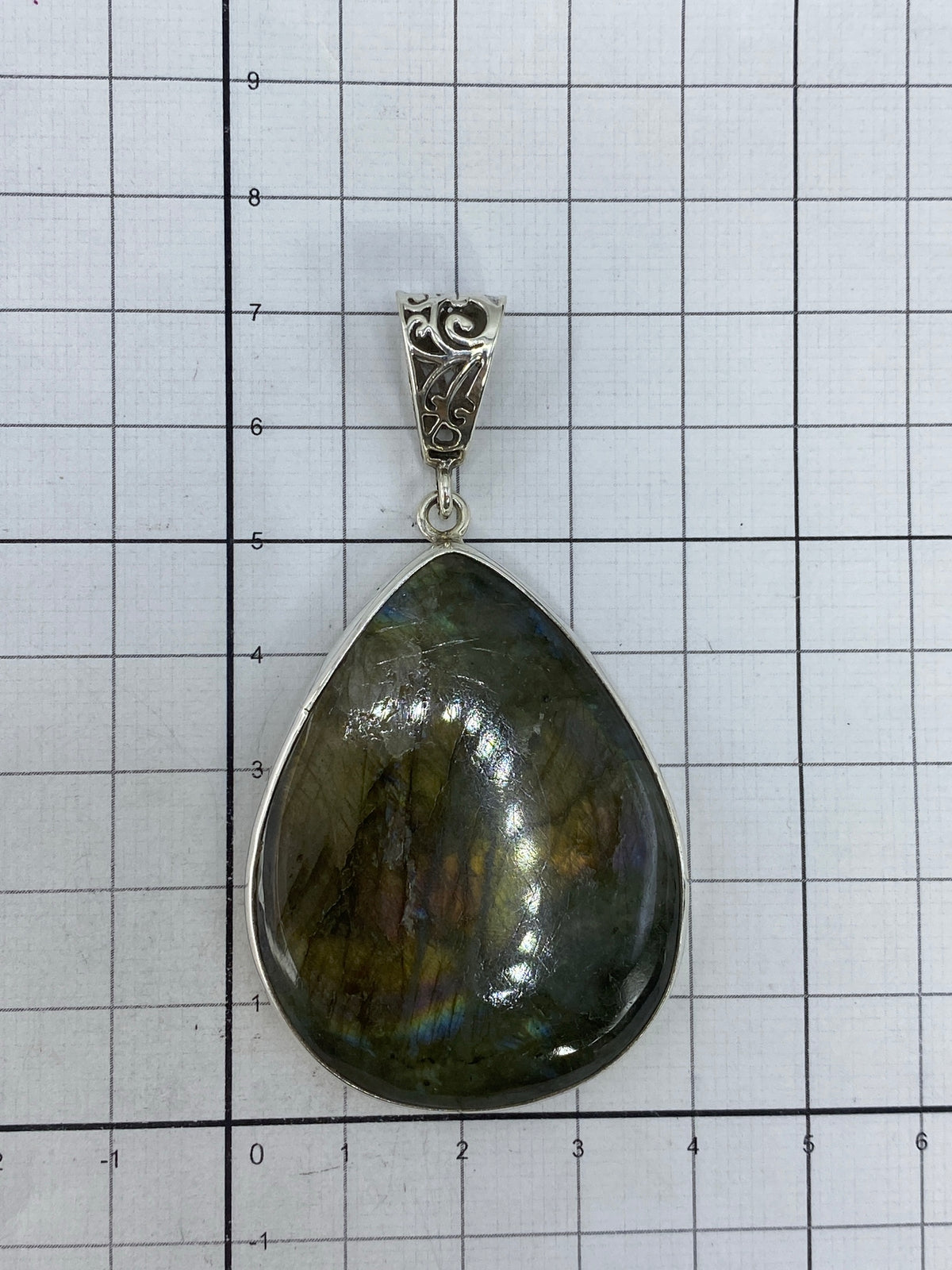 Dije de plata con piedra verde sobre regla de medición mostrando 7 centímetros