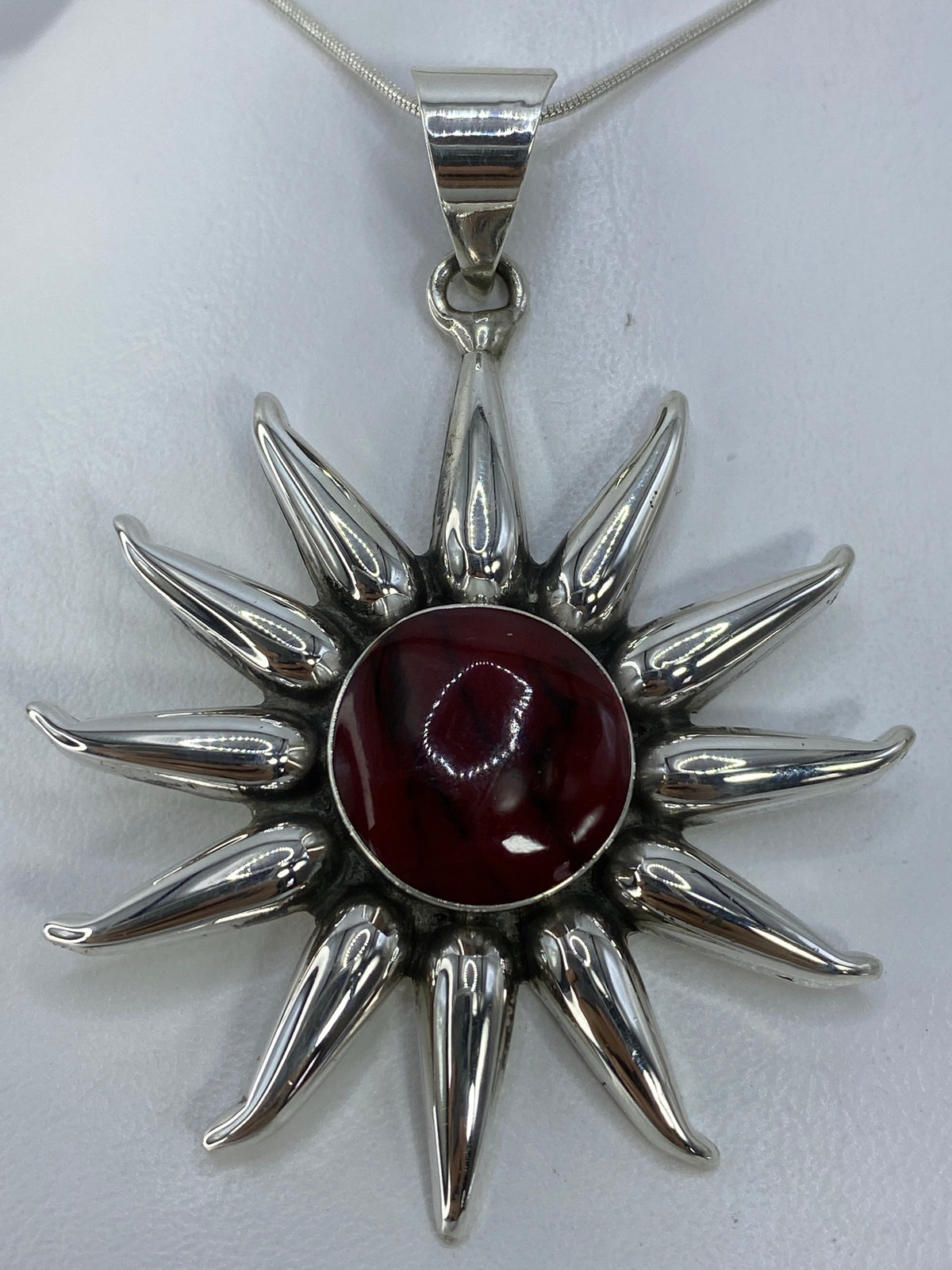Dije sol de plata 925 con piedra roja engastada en el centro, sobre fondo blanco