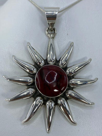 Dije sol de plata 925 con piedra roja engastada en el centro, sobre fondo blanco