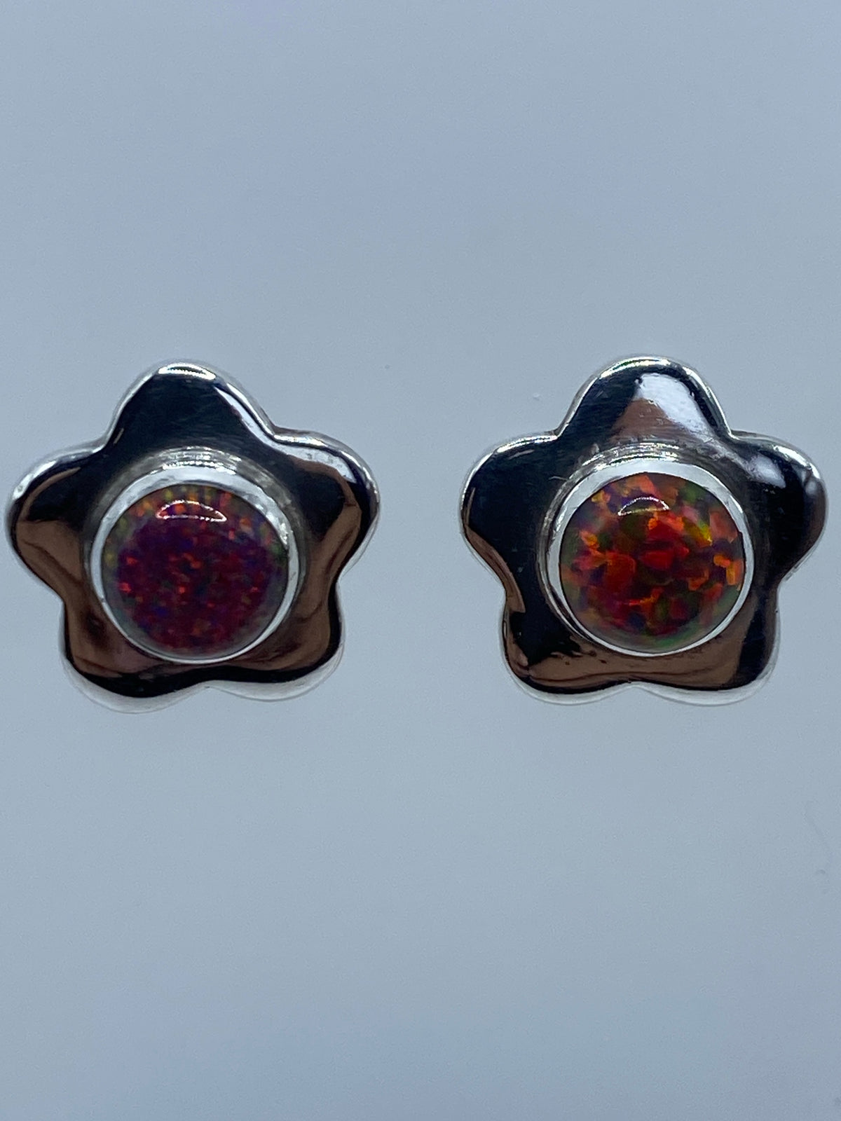 Detalle frontal de los aretes mostrando el ópalo de Fuego con tonos rojo, naranja y amarillo