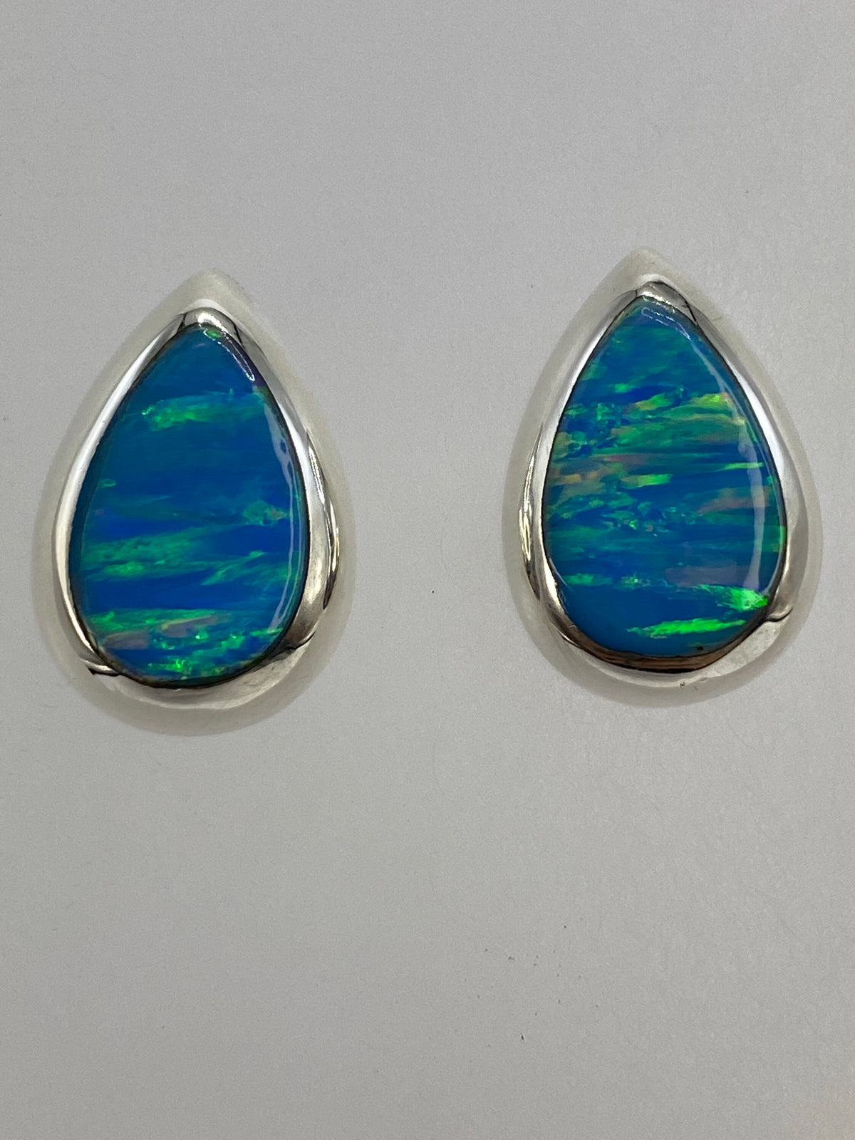 Aretes puestos sobre fondo azul mostrando los reflejos verdes del ópalo