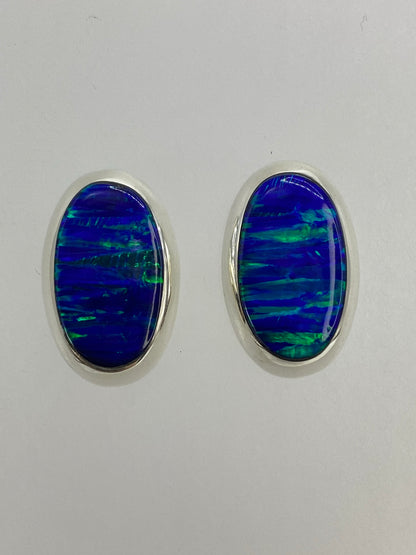 Par de aretes de plata con ópalo de fuego azul incrustado, sobre fondo blanco