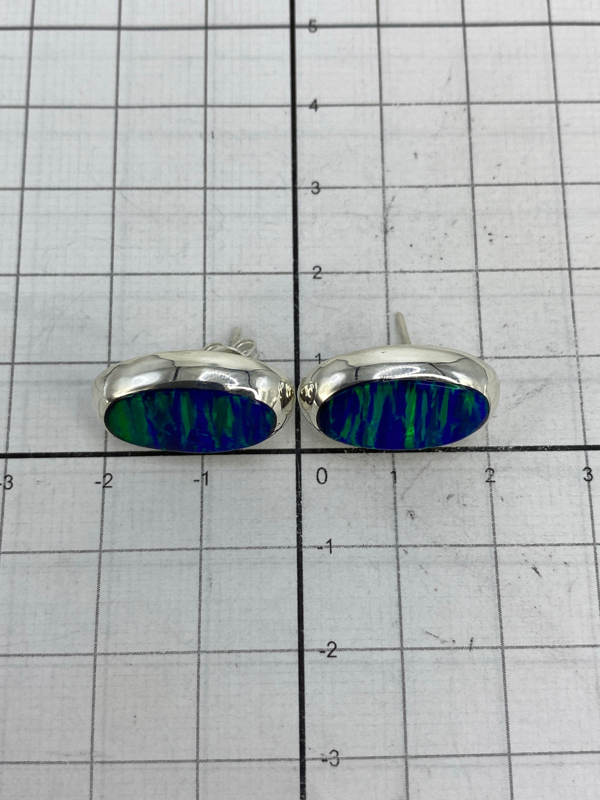 Aretes sobre regla métrica para mostrar tamaño (2 cm largo × 1.5 cm ancho)