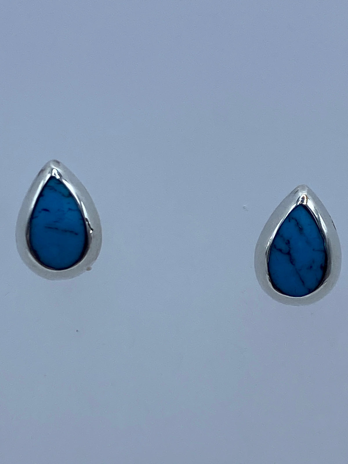 Detalle frontal de los aretes mostrando la turquesa engastada y el poste de plata