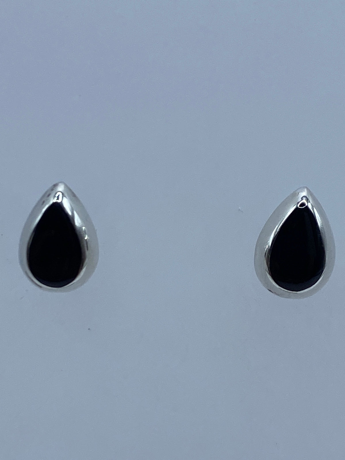 Aretes de plata 925 con ónix negro engastado, vistos de frente sobre fondo azul