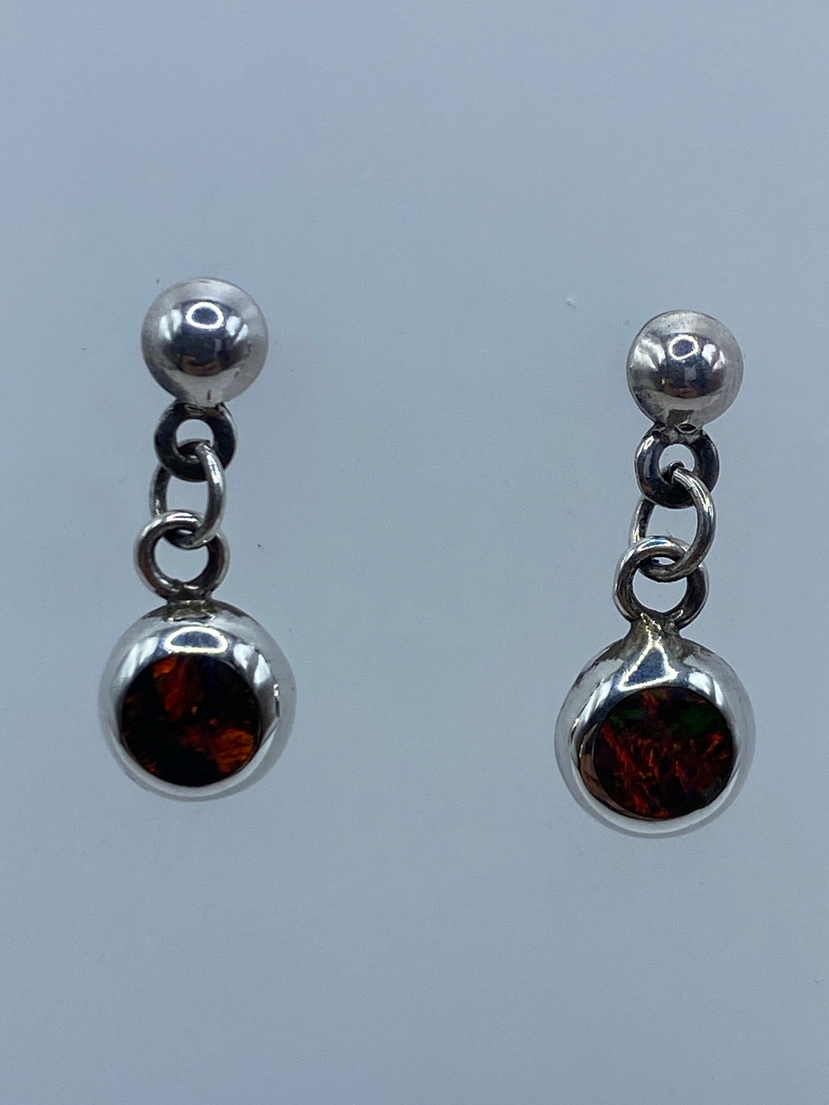 Par de aretes de plata con ópalo de fuego naranja rojizo, frente a fondo azul claro