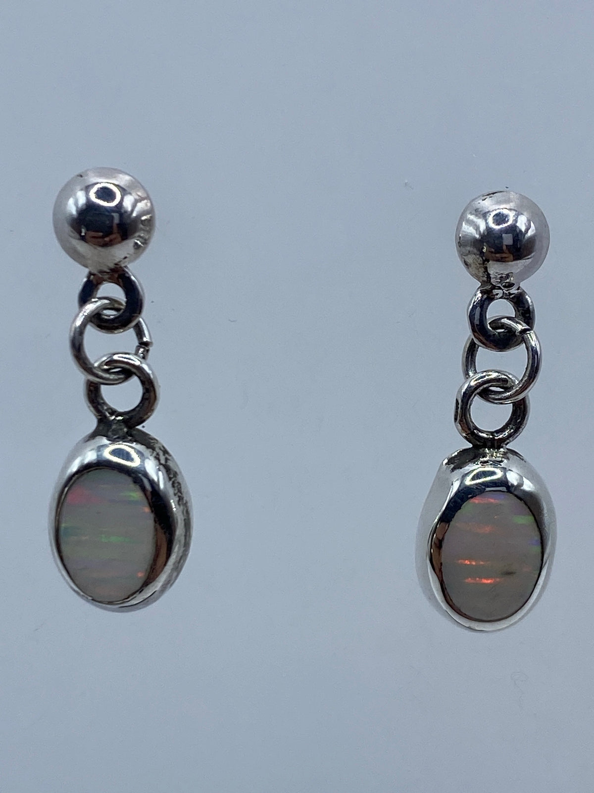 Par de aretes de plata 925 con ópalo de fuego multicolor, largos 2 cm, colgando sobre fondo gris