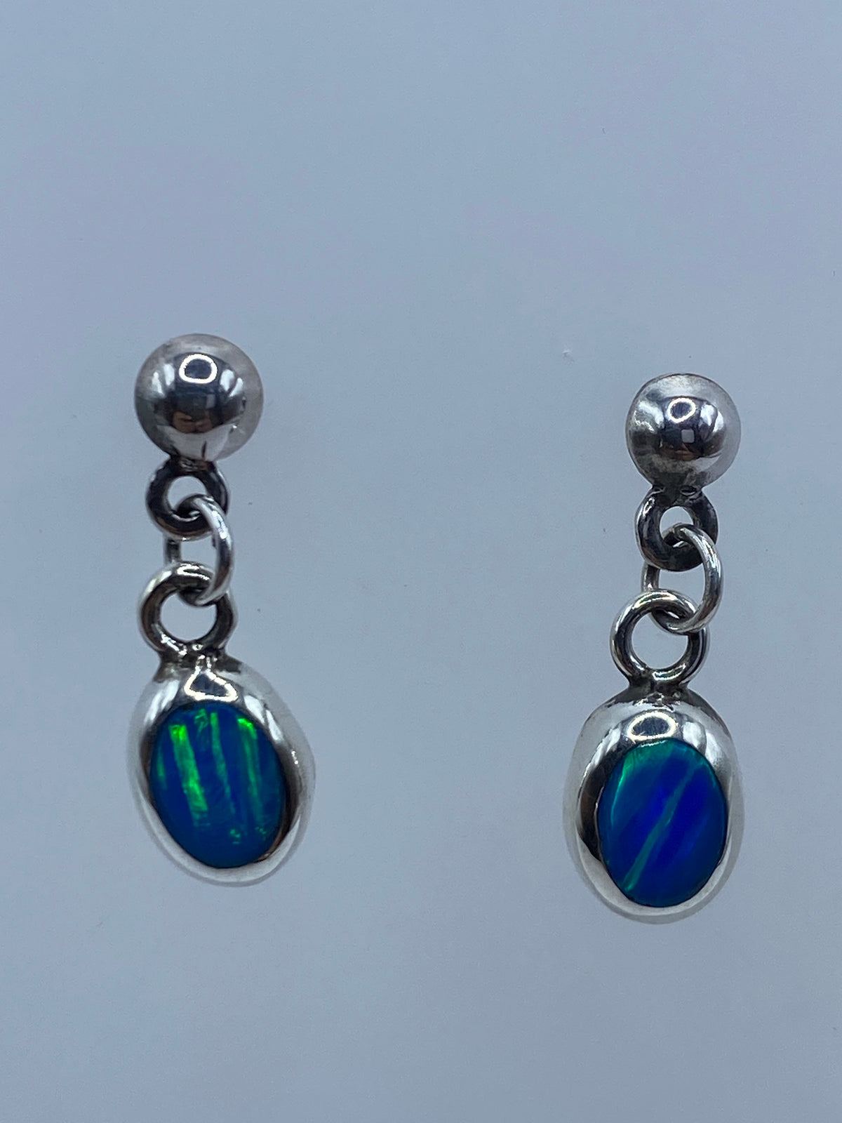 Par de aretes de plata 925 con ópalo de fuego azul engastado, colgando sobre fondo gris