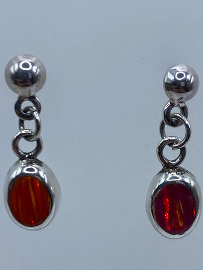 Aretes de ópalo de fuego colgantes en plata, mostrando el brillo naranja y rojo de la piedra