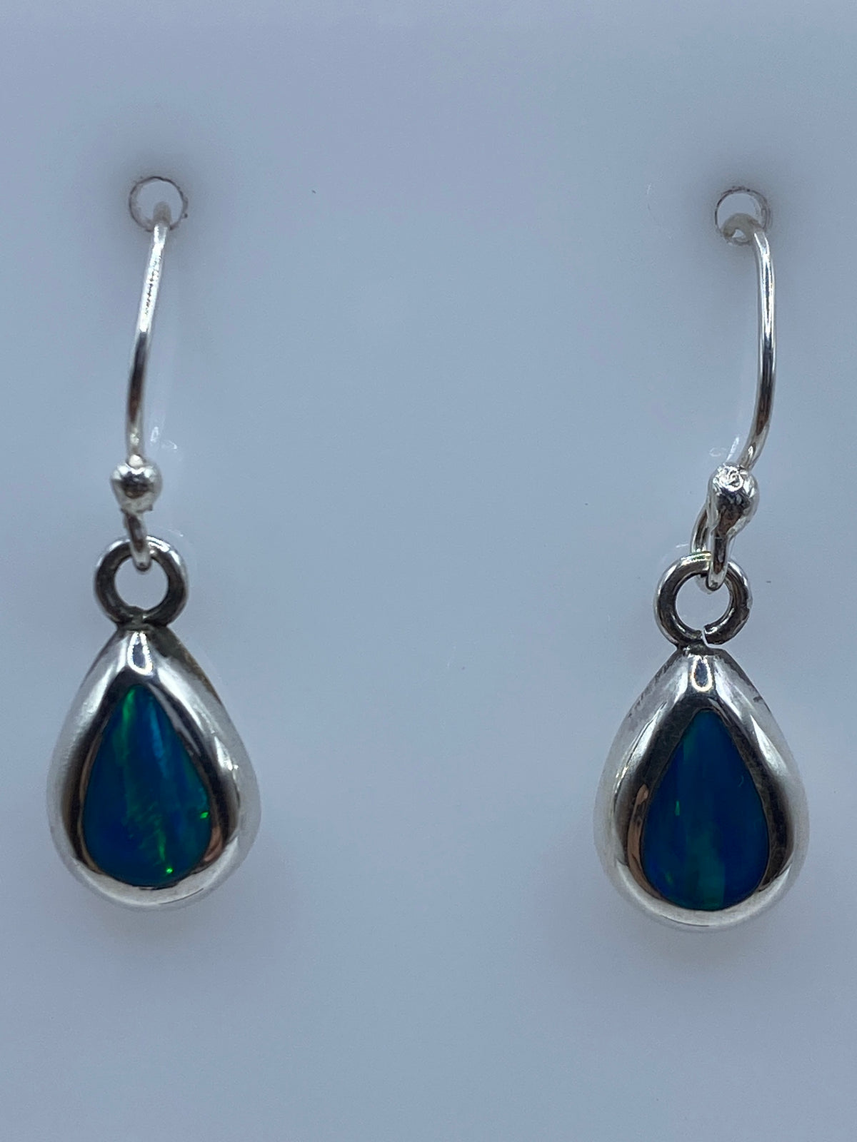 Par de aretes de plata 950 con ópalo de fuego azul, gancho visible, sobre fondo blanco