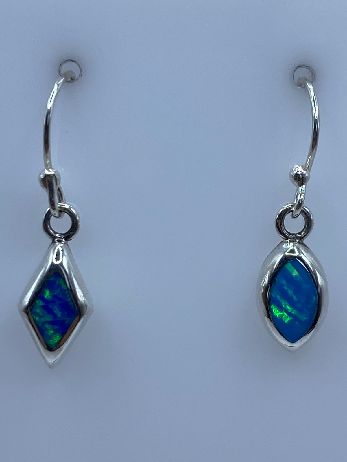 Par de aretes de plata con ópalo de fuego en tonos azul verdoso, colgando sobre fondo blanco