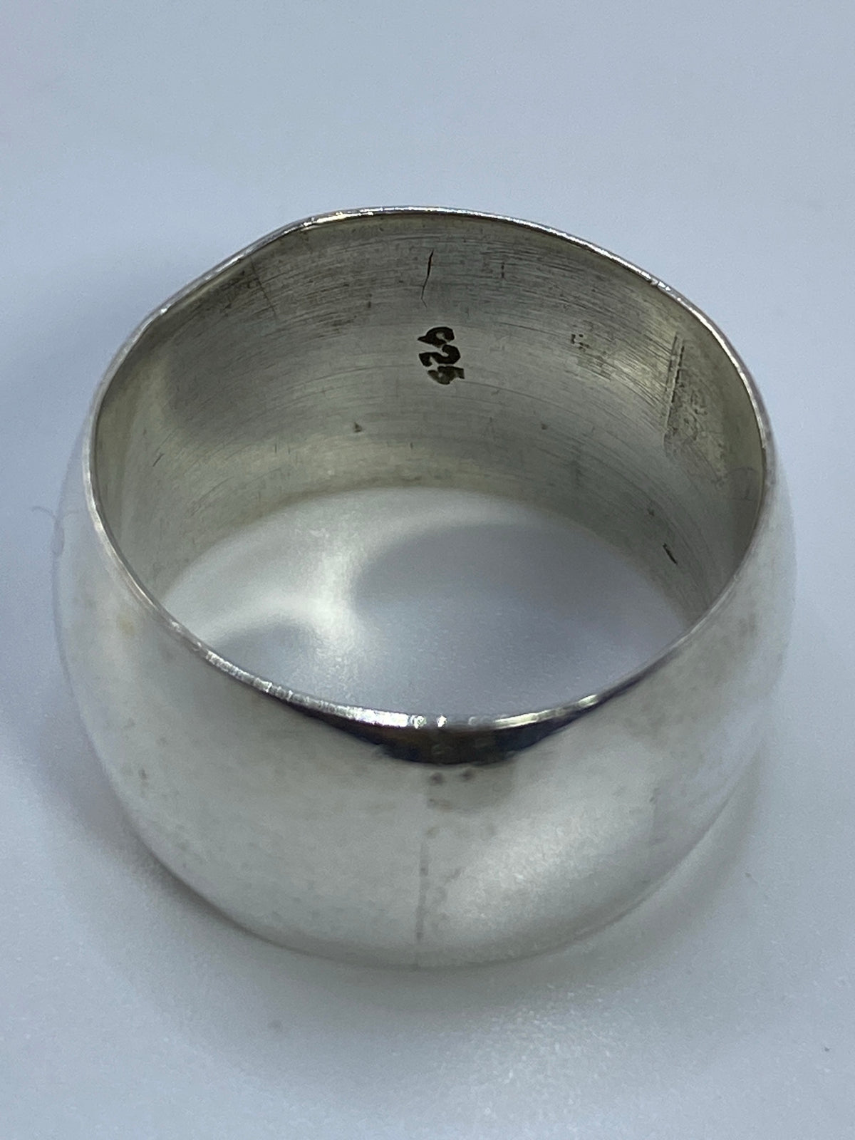 Anillo de plata minimalista en la mano, luz reflejada en su superficie pulida