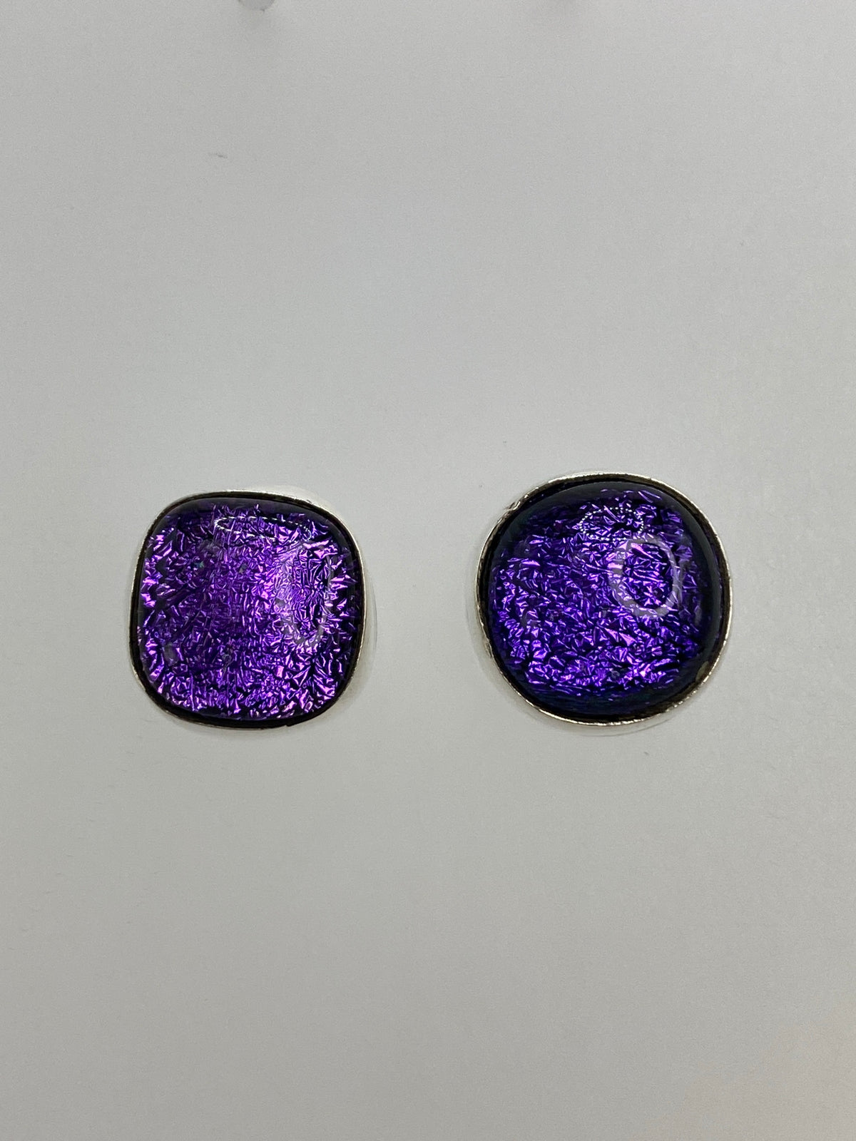 Par de aretes de plata 925 con piedra morada engastada, frente a fondo blanco