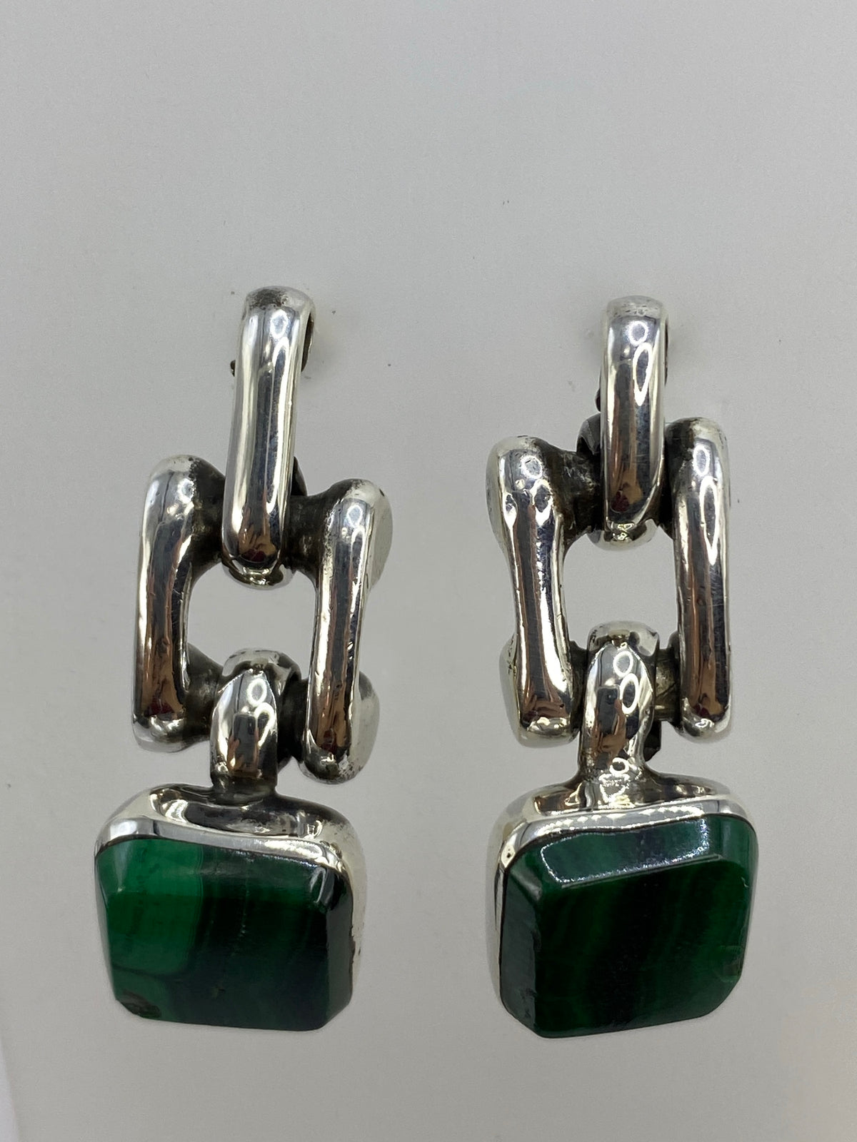 Arete de malaquita mostrando las vetas verde profundo y el marco escultórico de plata