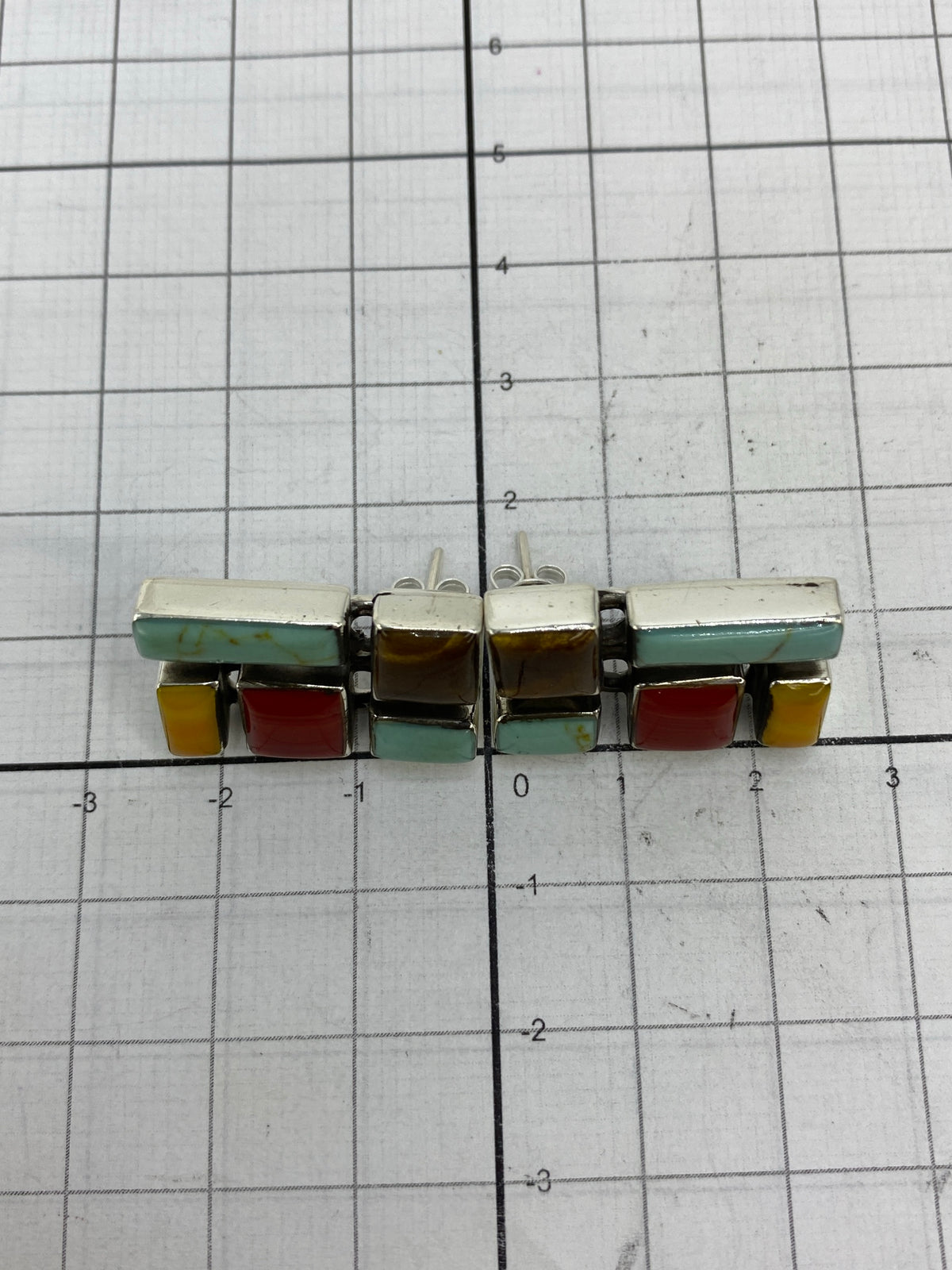 Aretes en la mano mostrando tamaño de 2.4 cm de largo y la combinación de colores
