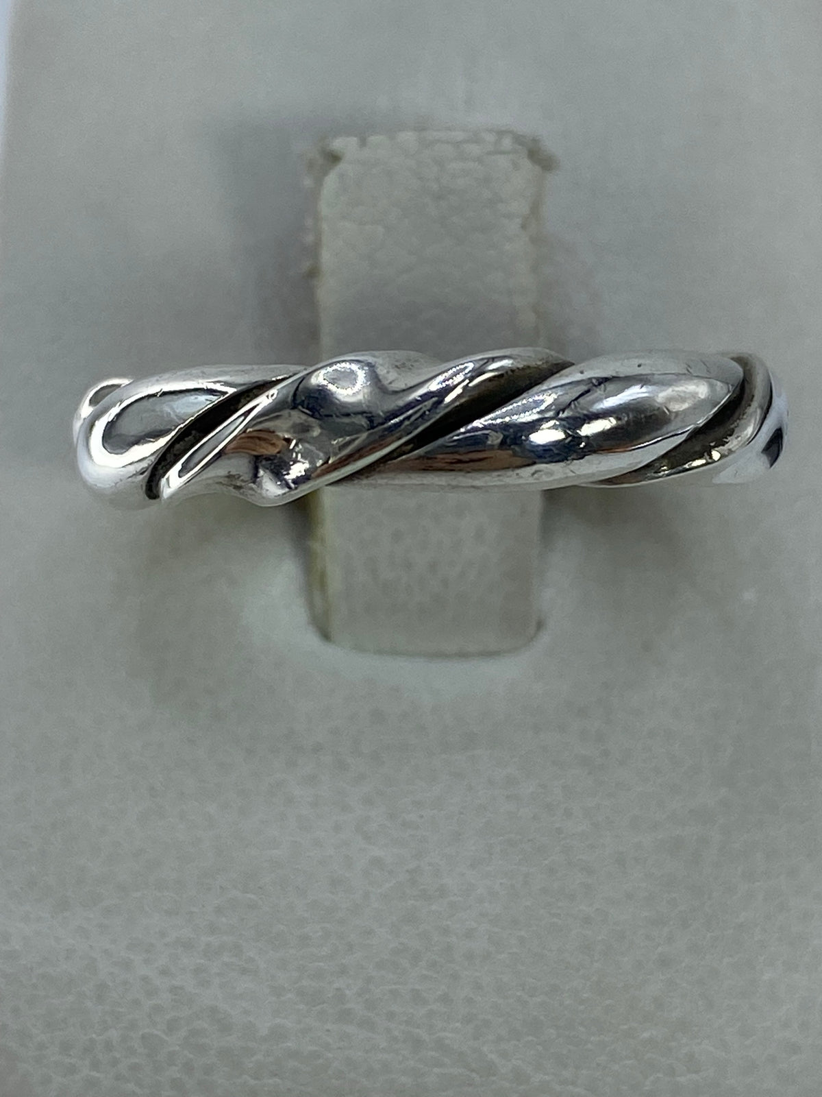 Anillo de plata eslabón torcido en la mano sobre fondo neutro