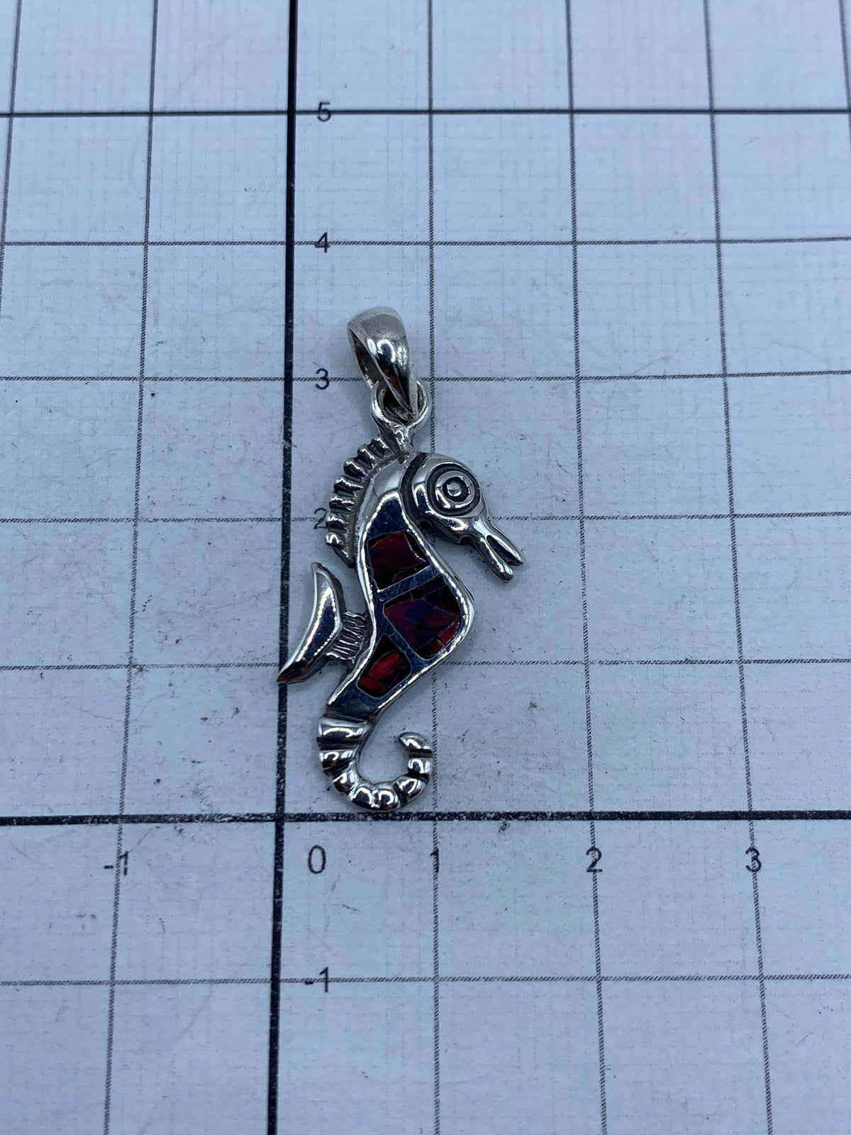 Dije de caballito de mar sobre medidor de centímetros, mostrando tamaño real de 3.3 cm