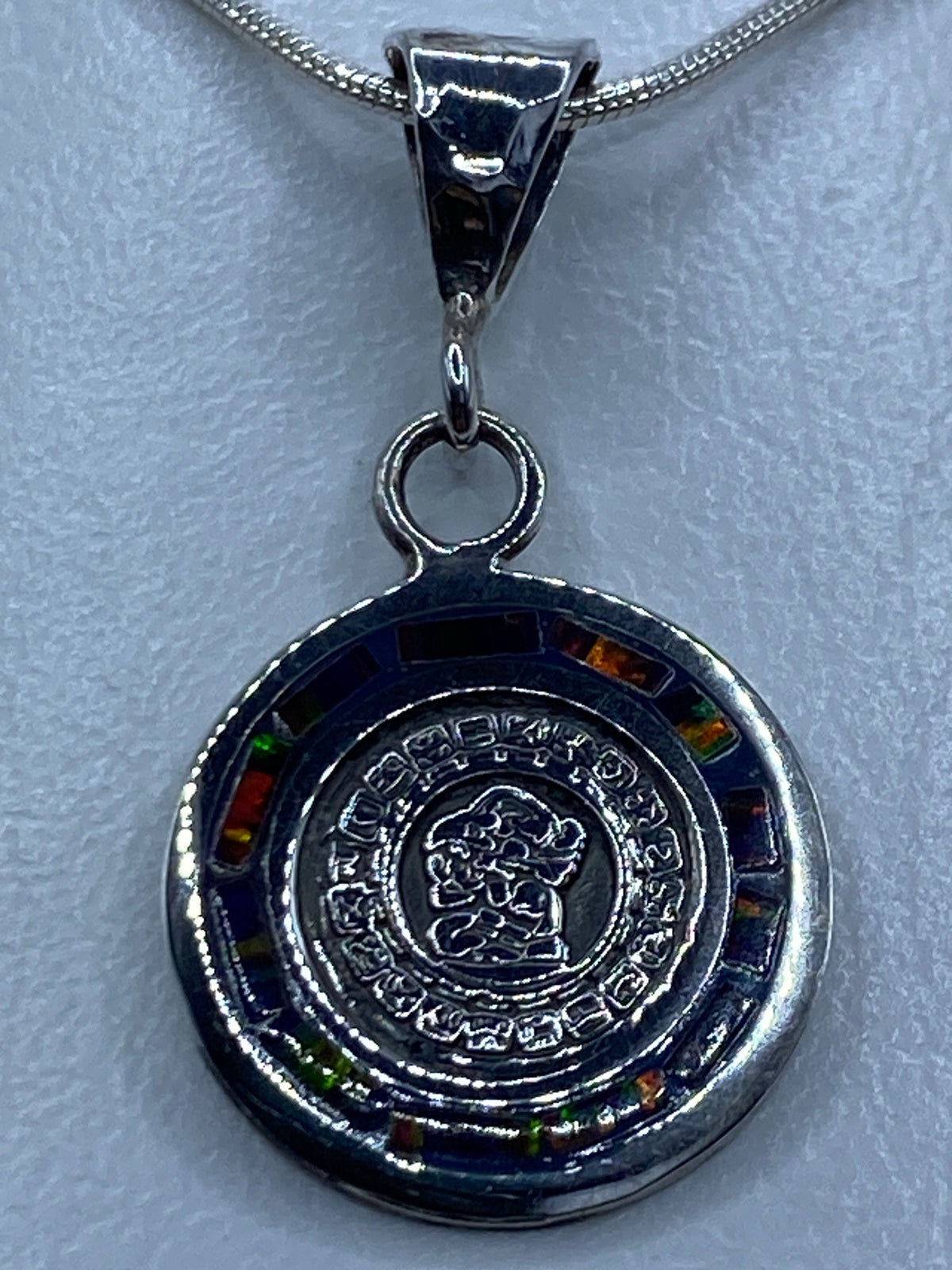 Dije de plata con ópalo de fuego multicolor en diseño del Calendario Maya, colgante sobre cadena plateada